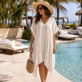 Woman in a white cover-up and straw hat by a pool with palm trees in the background