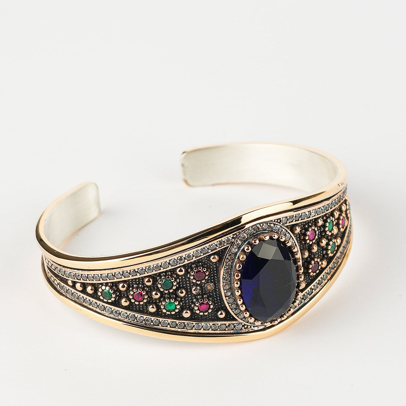 Decorative bracelet with a central blue gemstone and multicolored stones on a white background