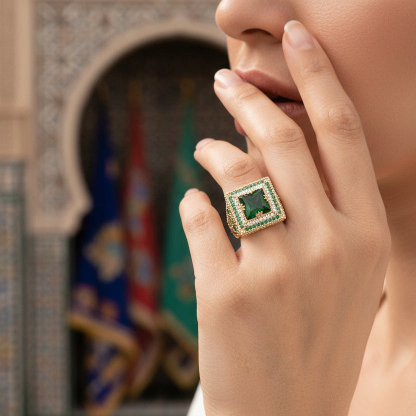 Gold ring with a green gemstone on a hand against a white background
