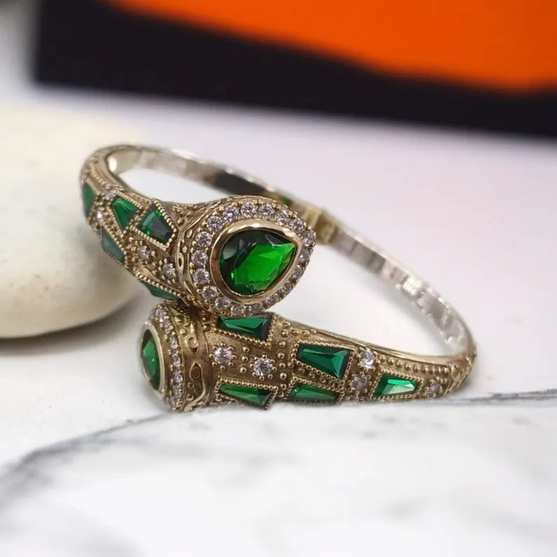 Gold bracelet with green gemstones on a marble surface