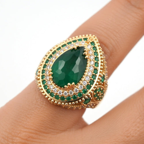 Gold ring with a green gemstone on a finger against a white background