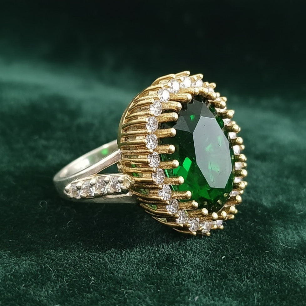 Gold ring with a green gemstone on a green fabric background