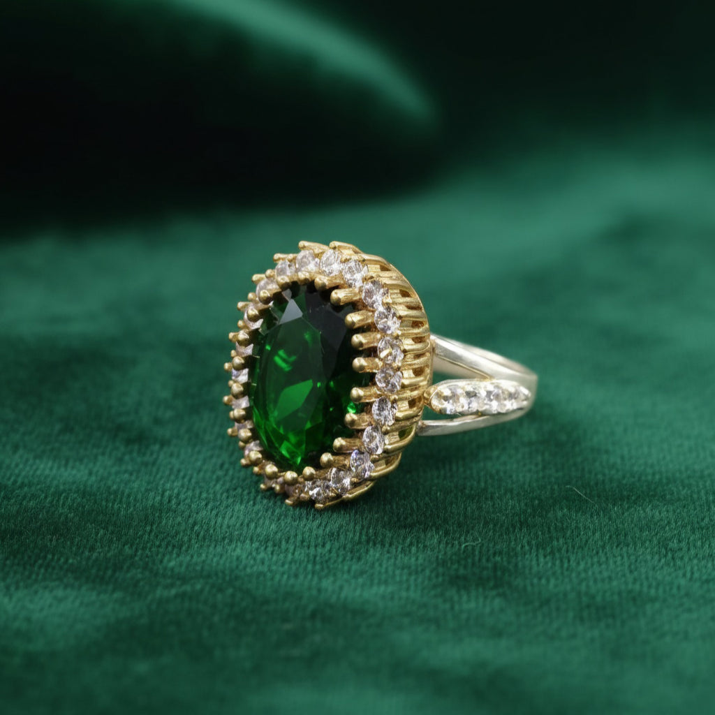 Gold ring with a green gemstone on a green fabric background