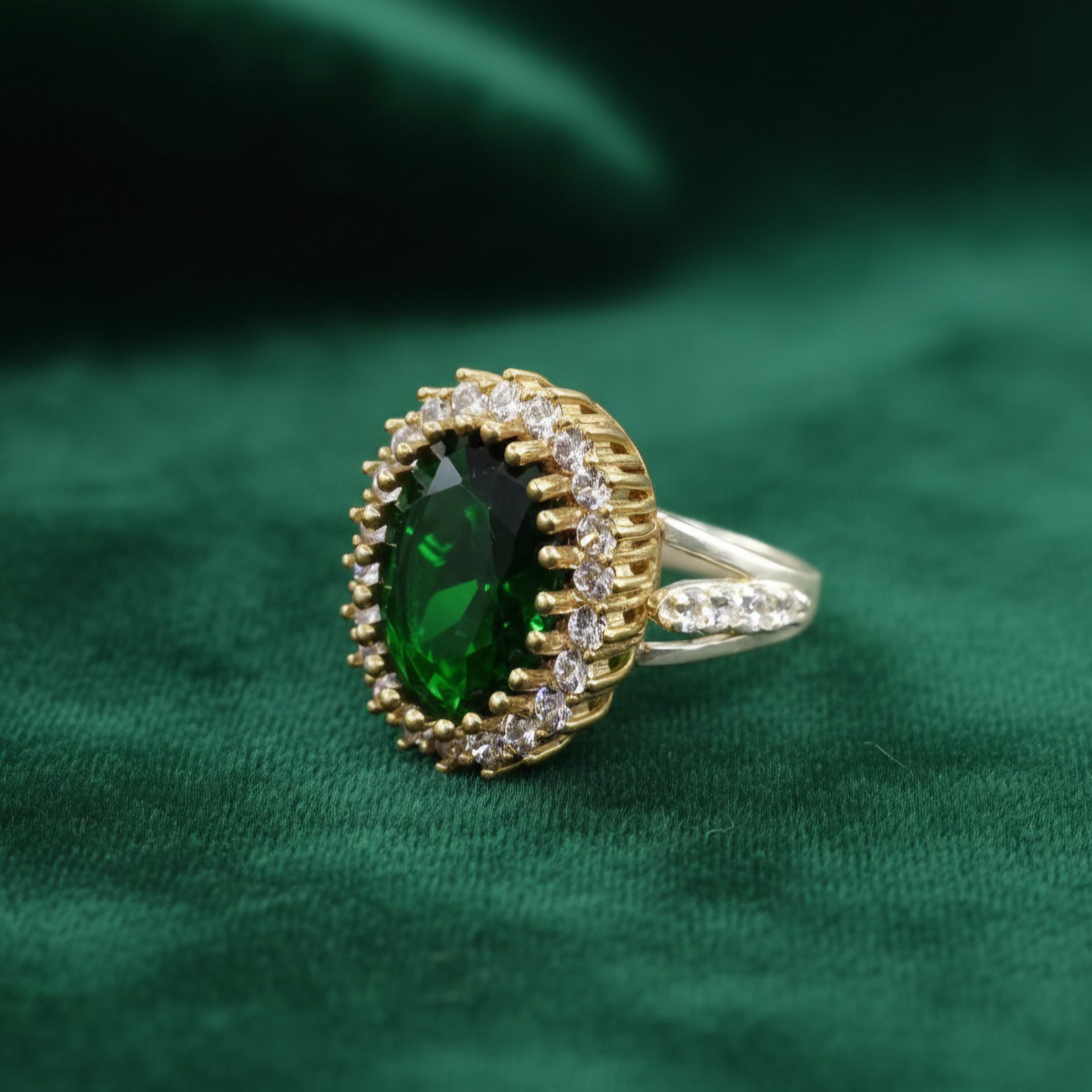 Gold ring with a green gemstone on a green fabric background