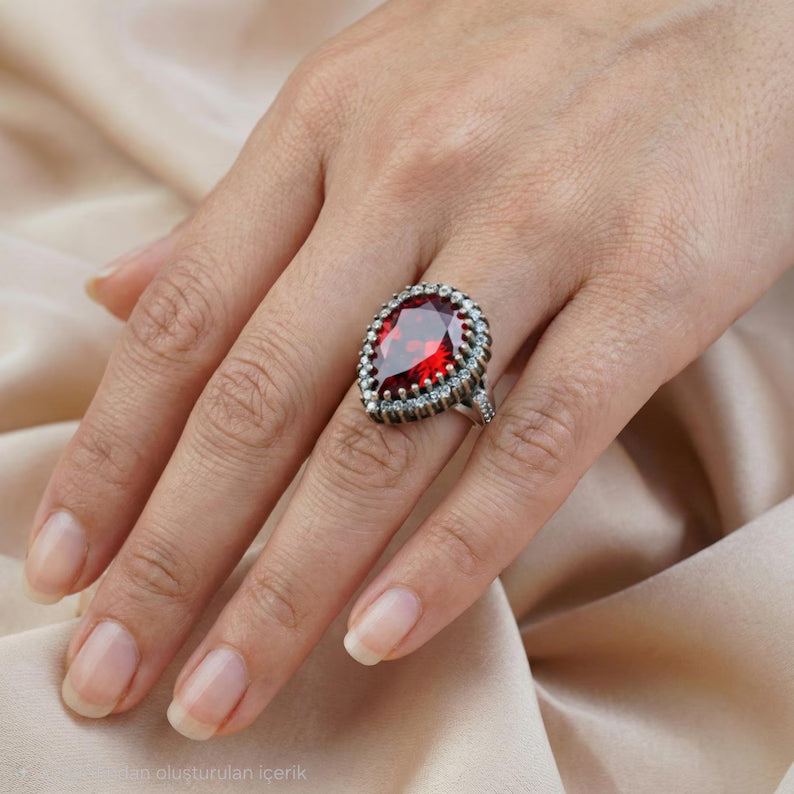 Close-up of a hand wearing a ring with a red gemstone on a beige fabric background